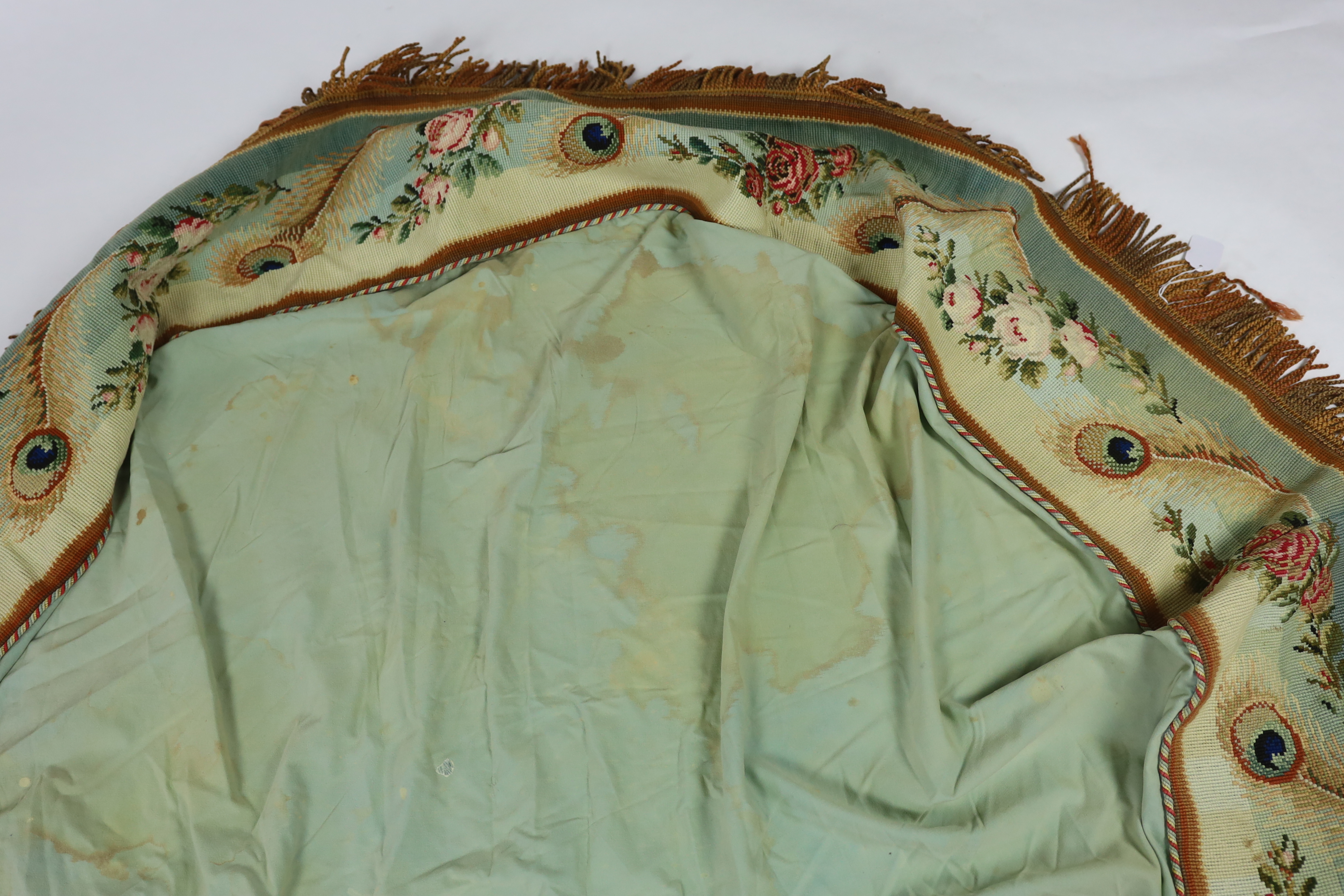 A 19th century Berlin hand wool worked floral and peacock feather designed border, with a deep fringe and cording along the top edge, used as the outer edge/border to a plain cotton turquoise table cover, the wool work a